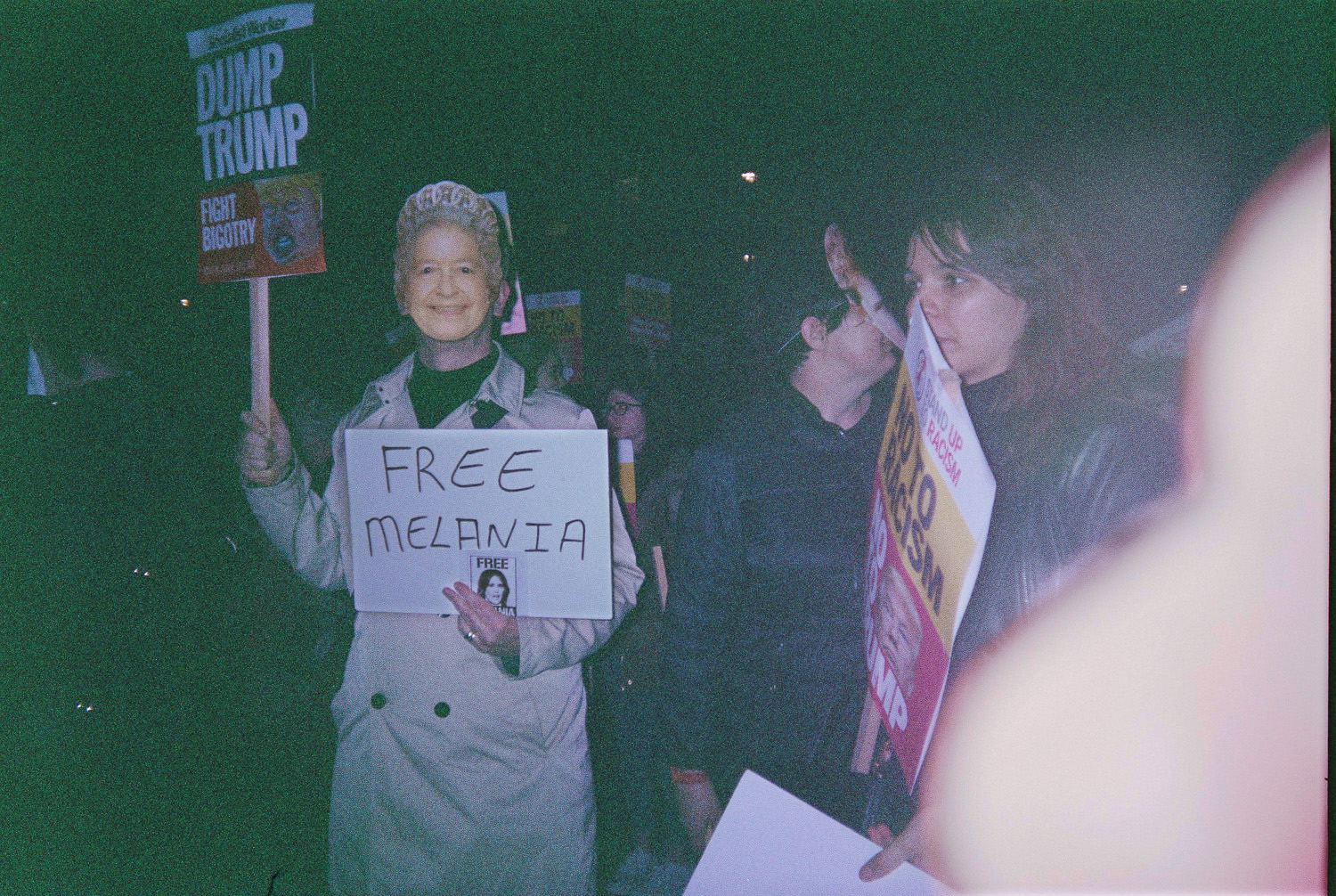 person with Queens face mask holding sign that reads "free Melania"
