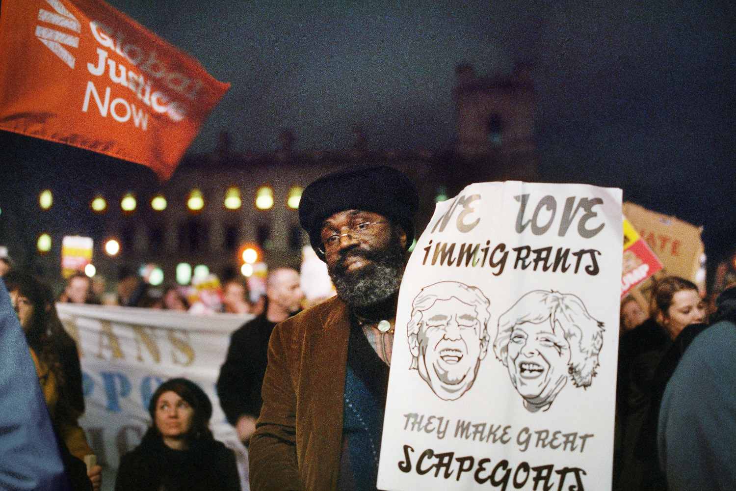 Black man holding placard with the faces of Trump and Theresa May 