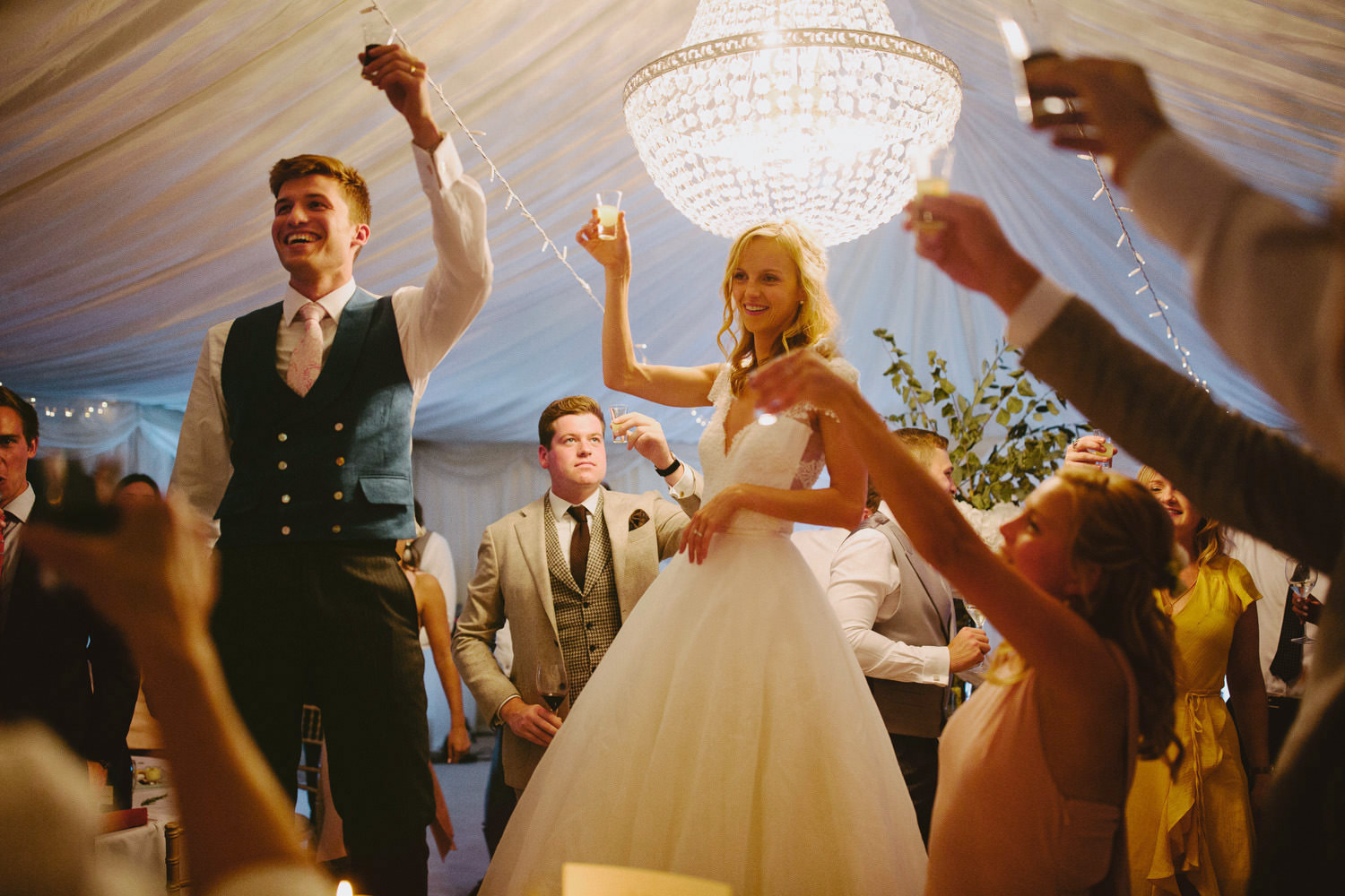 bride and groom stood on chair with toast holding glasses aloft