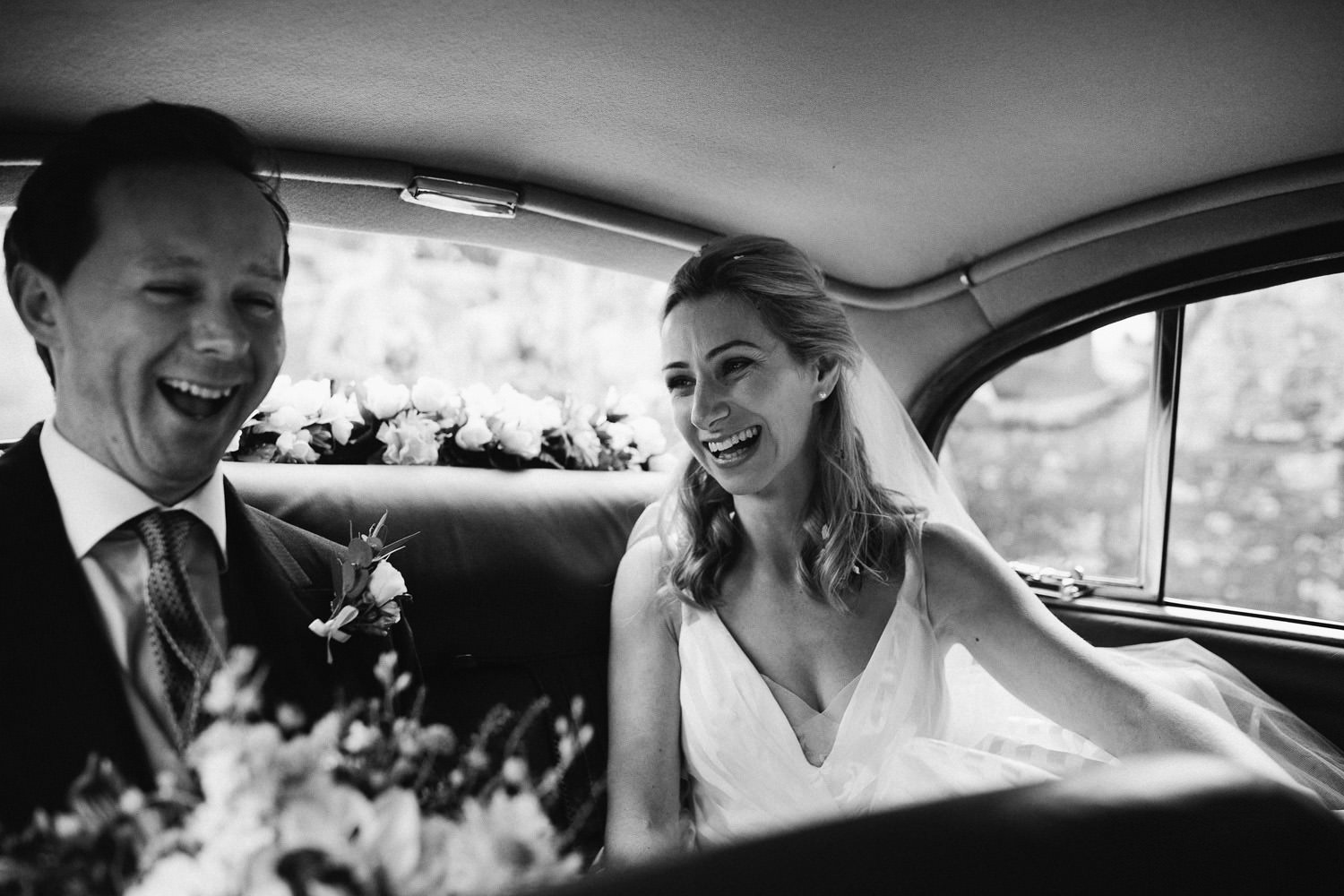bride and groom laugh in back of car 