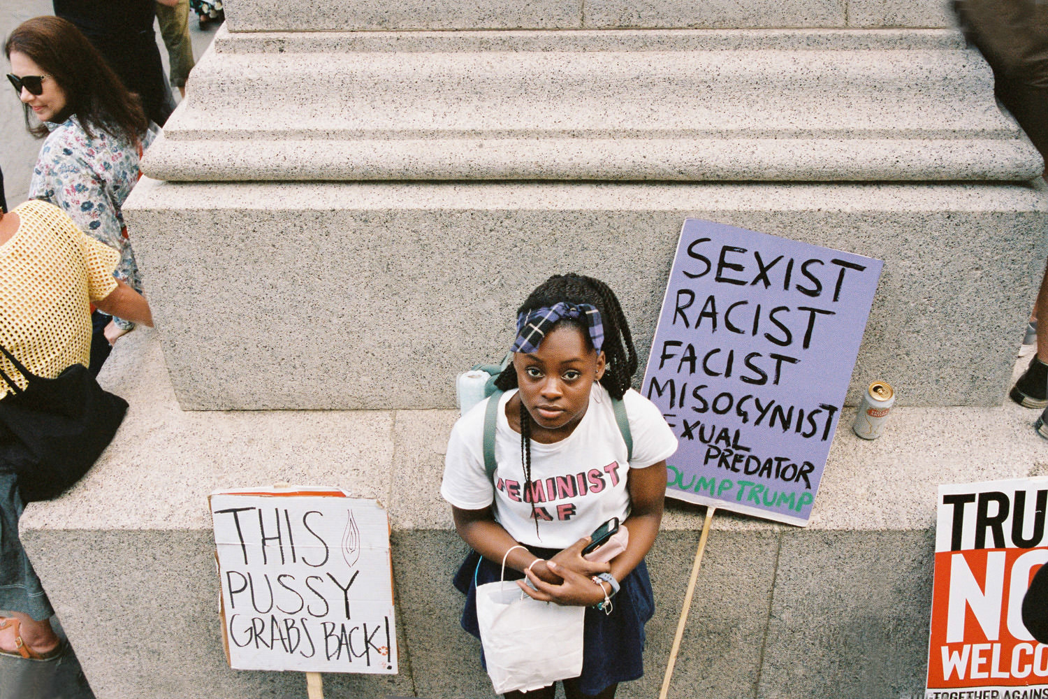 black girl looking into lens with two placards at London Trump protest