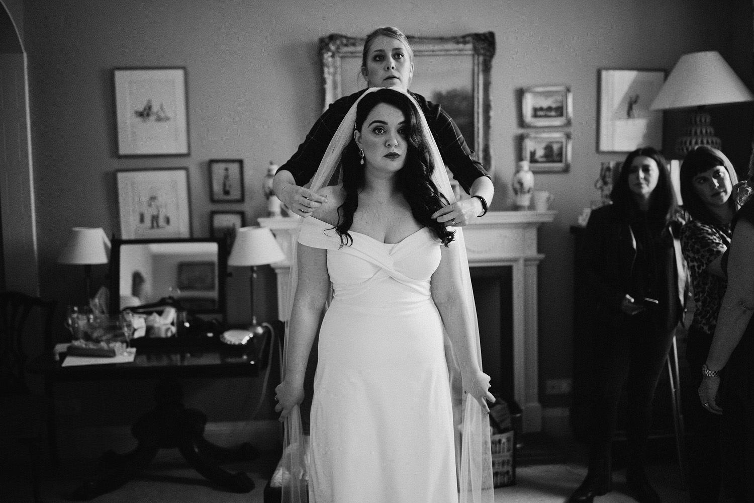 friend adjust veil while bride faces the mirror